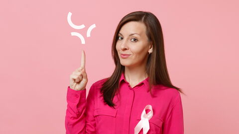 Une femme porte un ruban rose (Octobre Rose) sur sa chemise fuchsia et pointe du doigt le sigle blanc de l'UPHF.